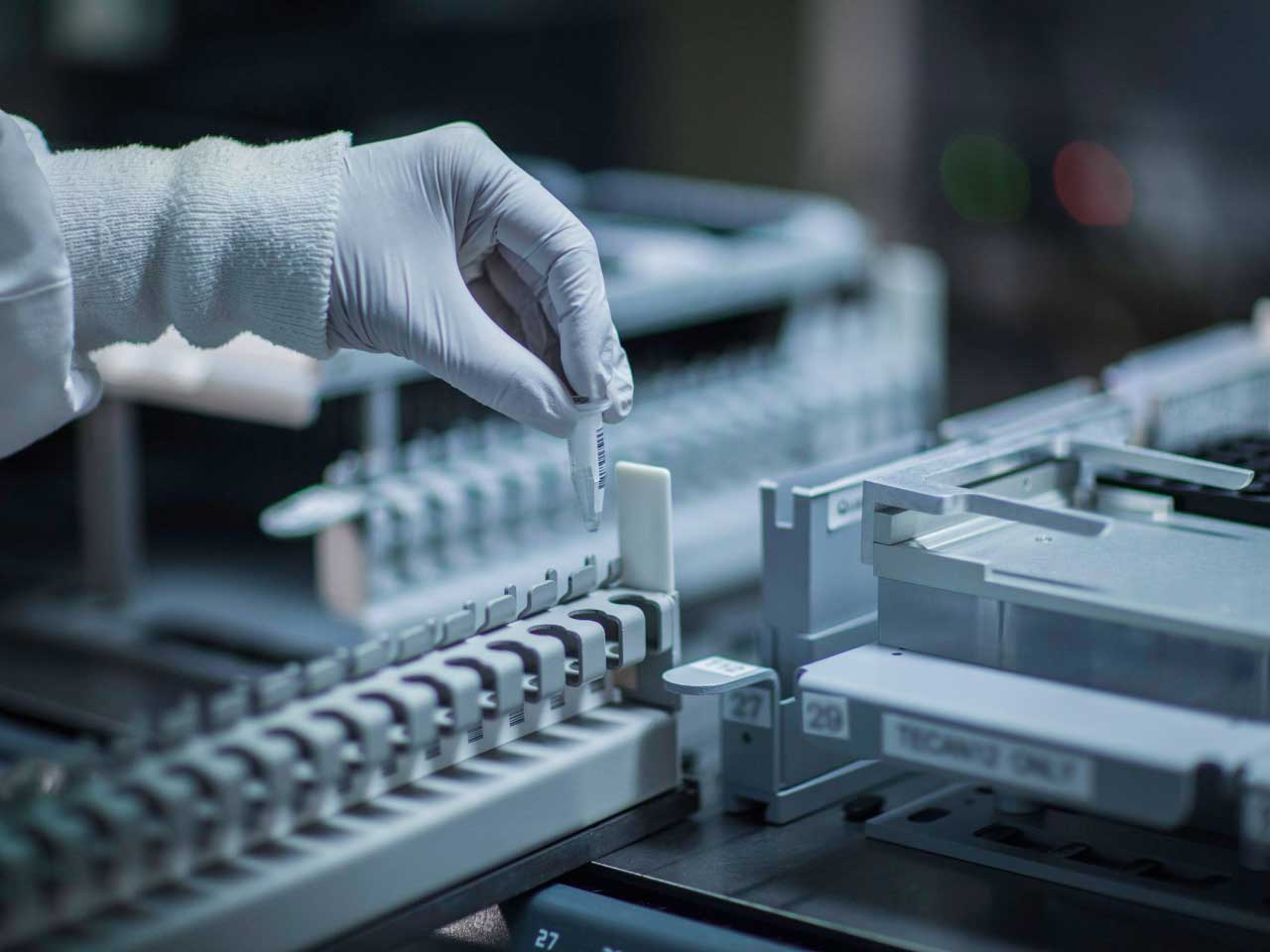 A lab technician's hand placing a test tube into lab equipment.