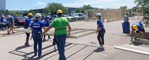 a group of people in hard hats carrying a piece of a house frame