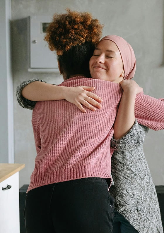Two women hugging. One is a chemotherapy patient and is smiling softly.
