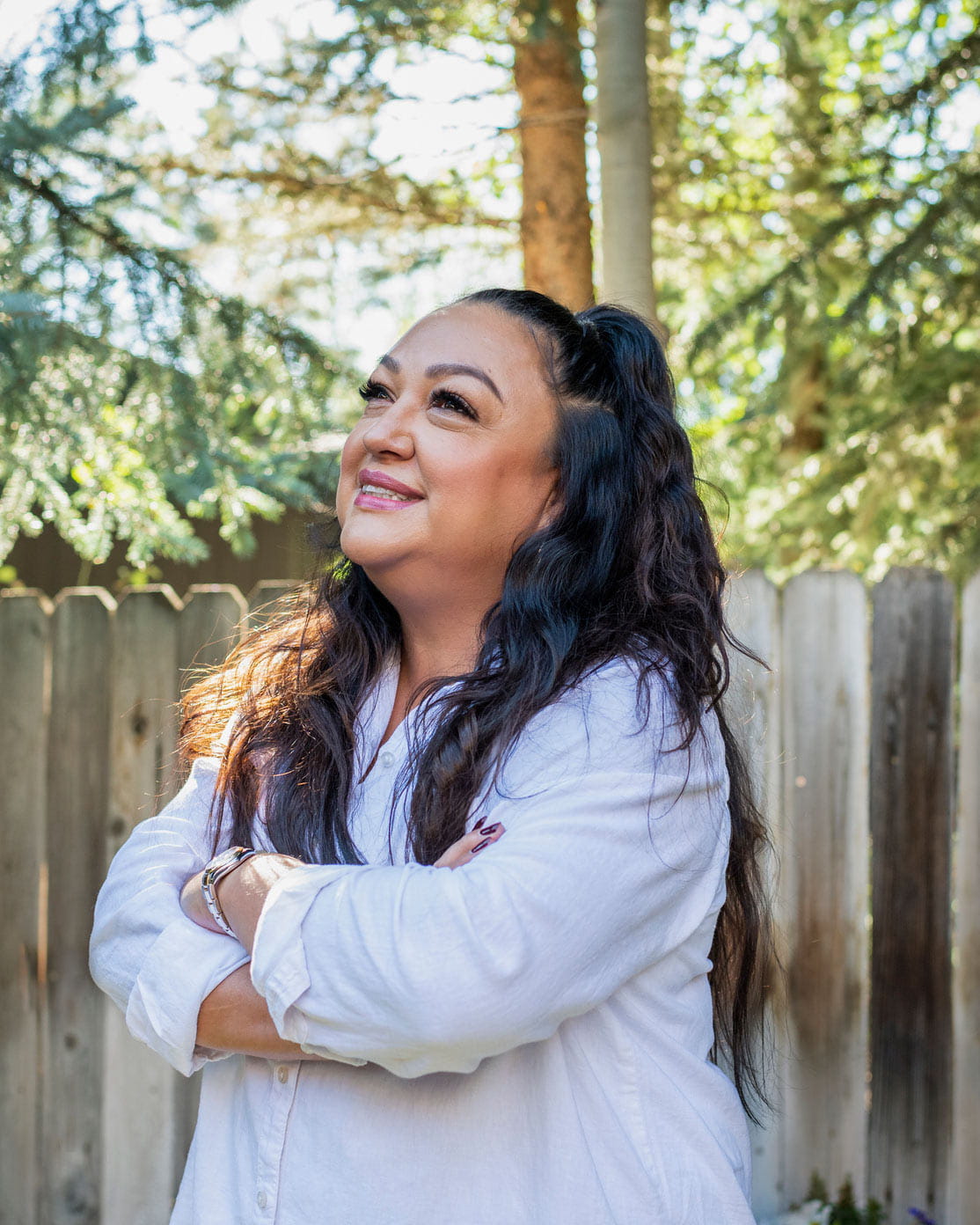 A woman smiling and gazing off into her sunny yard.
