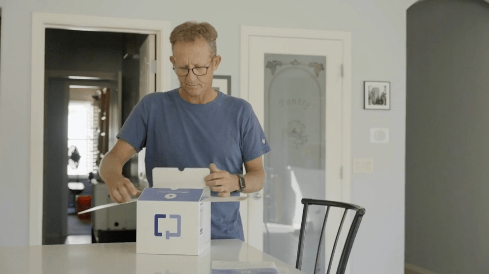 A patient opening a Cologuard box at a dining table A patient opening a Cologuard box at a dining table