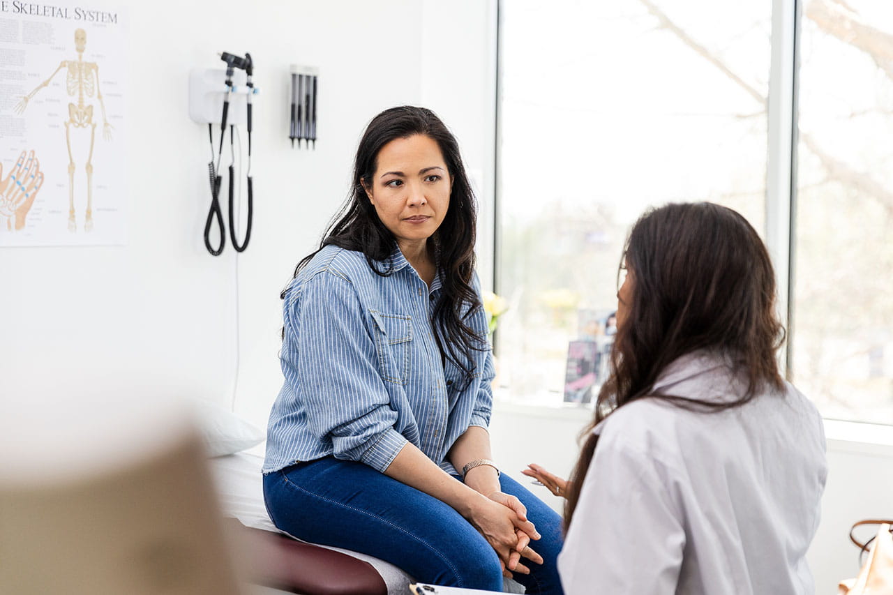 Healthcare provider discussing CRC screening with a patient who is sitting on an exam table.