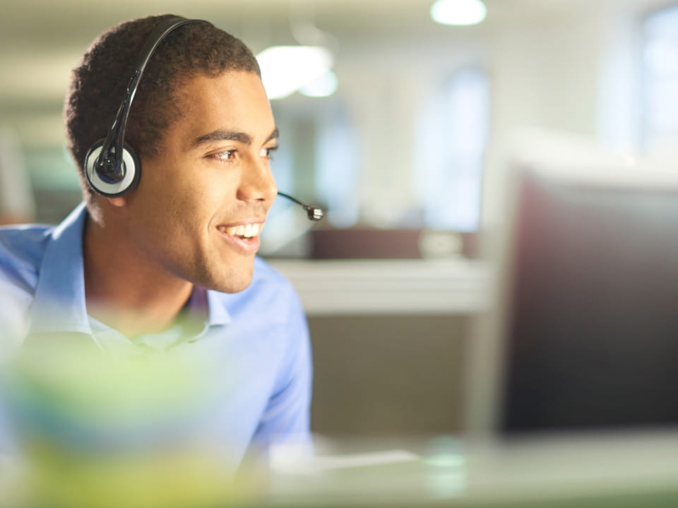 Smiling customer service representative talking to someone with a headset on.