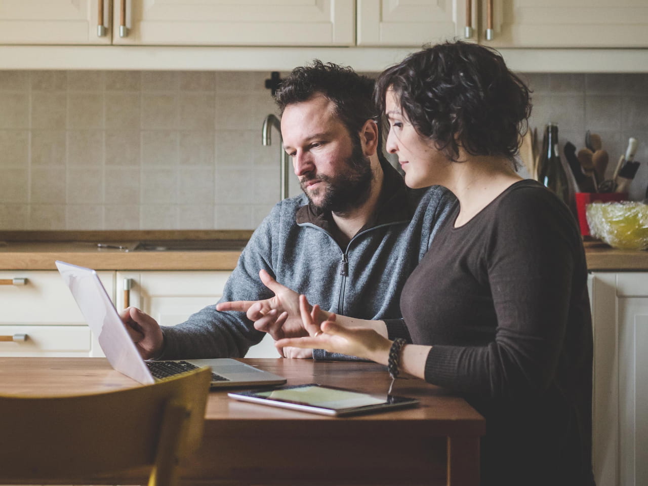 Couple sitting at a kitchen table reviewing information on a laptop.