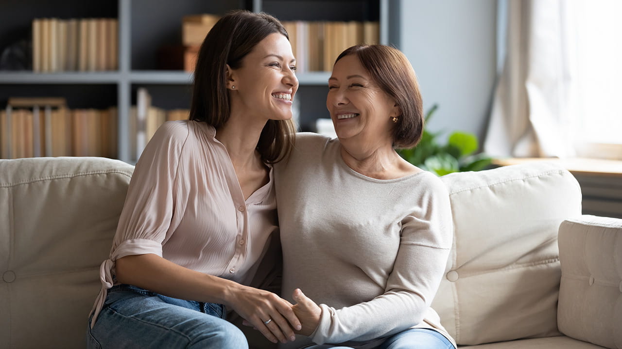 Two women smiling and hugging each other on a couch.