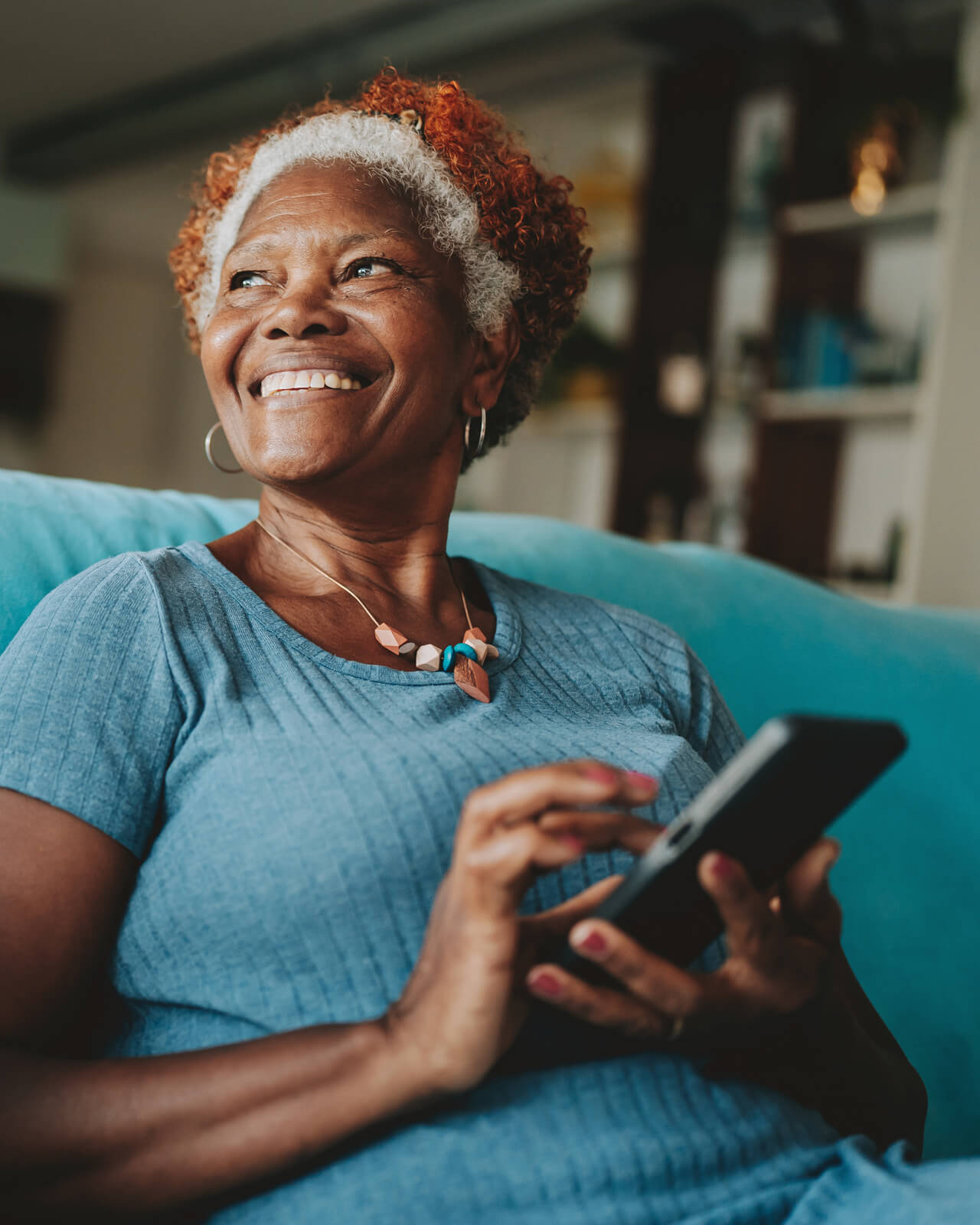 A woman sitting on a couch, smiling and using a smartphone.