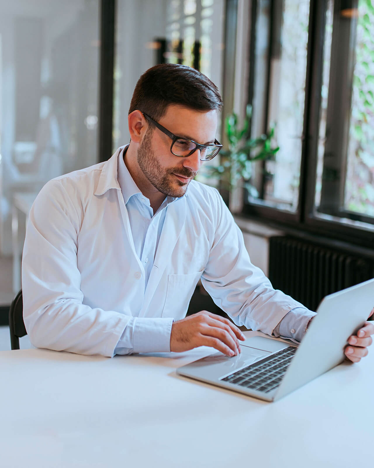 A doctor sitting at a desk looking at a laptop.