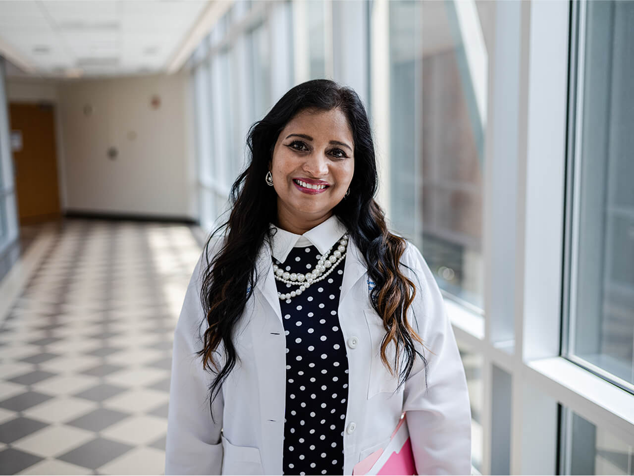 Deepa wearing a doctor’s jacket and smiling.