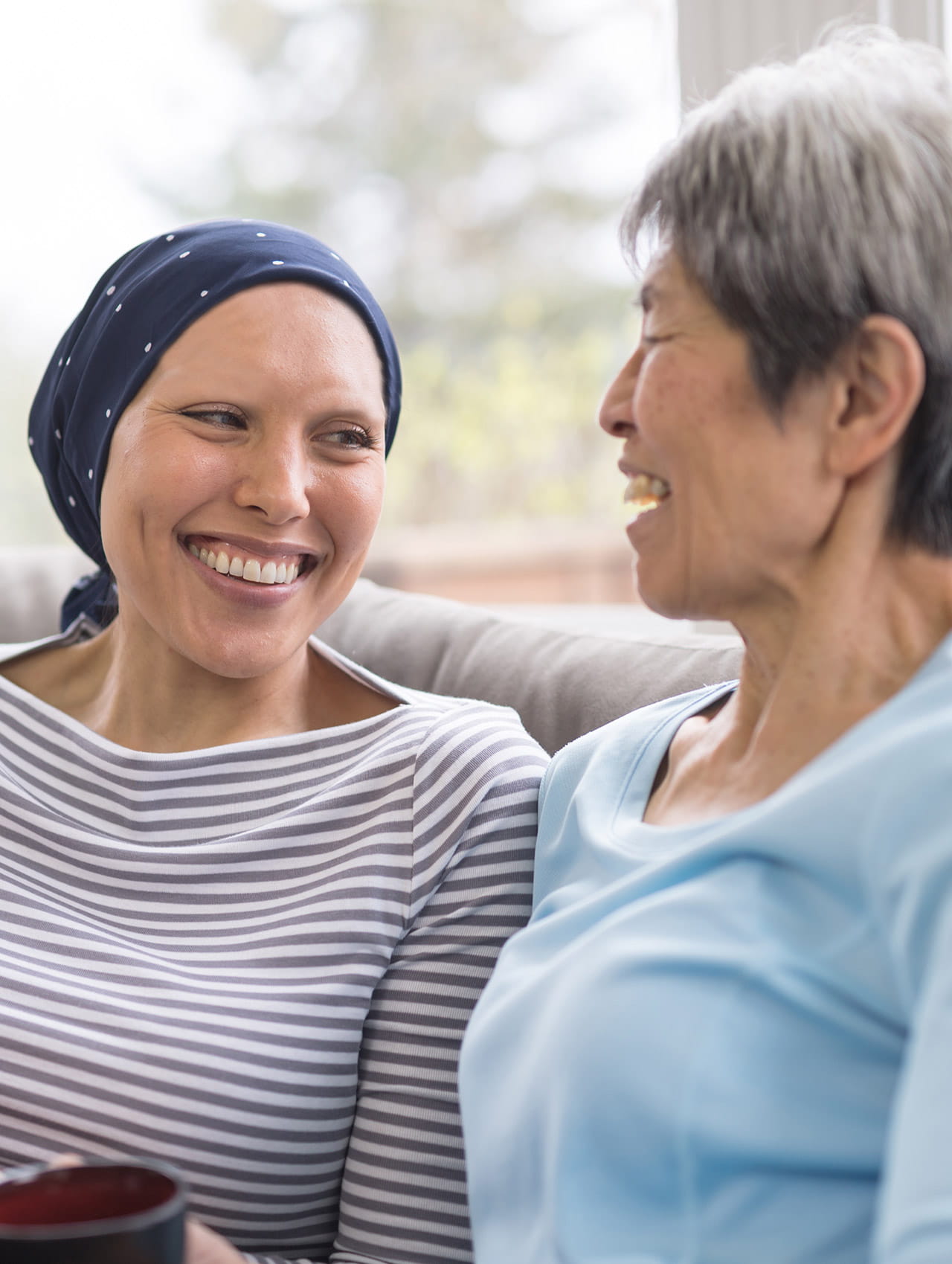 Two women sitting on a couch smiling at each other.