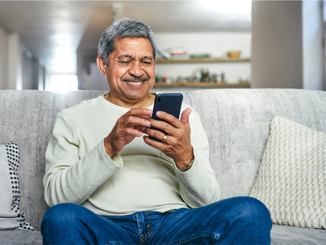 A man sitting on a couch smiling and looking at his smartphone.