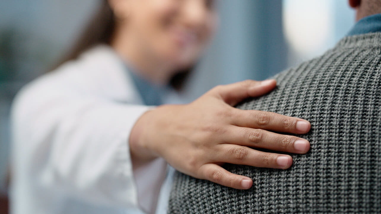A healthcare provider placing their hand on a patient’s back.