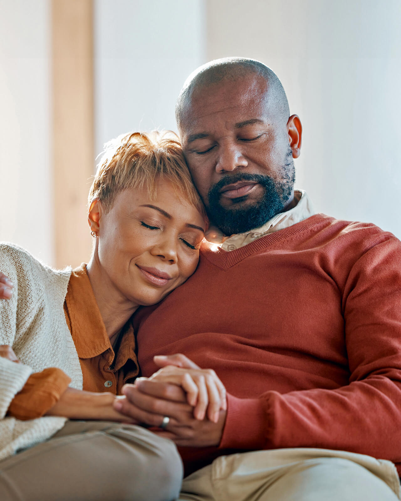 A man and woman sitting together with their eyes closed, holding hands.