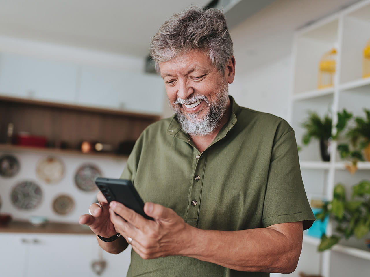 A bearded man smiling and looking at his smartphone.